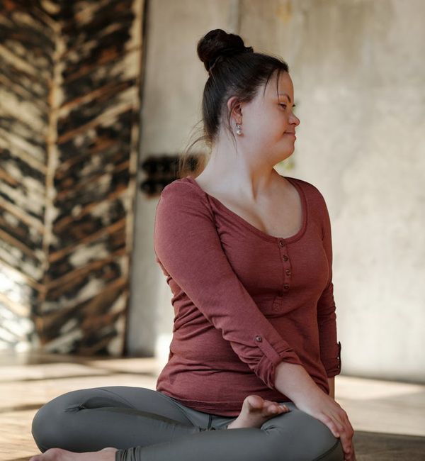 Woman practicing a gentle stretch in a calm, soft-lit room.